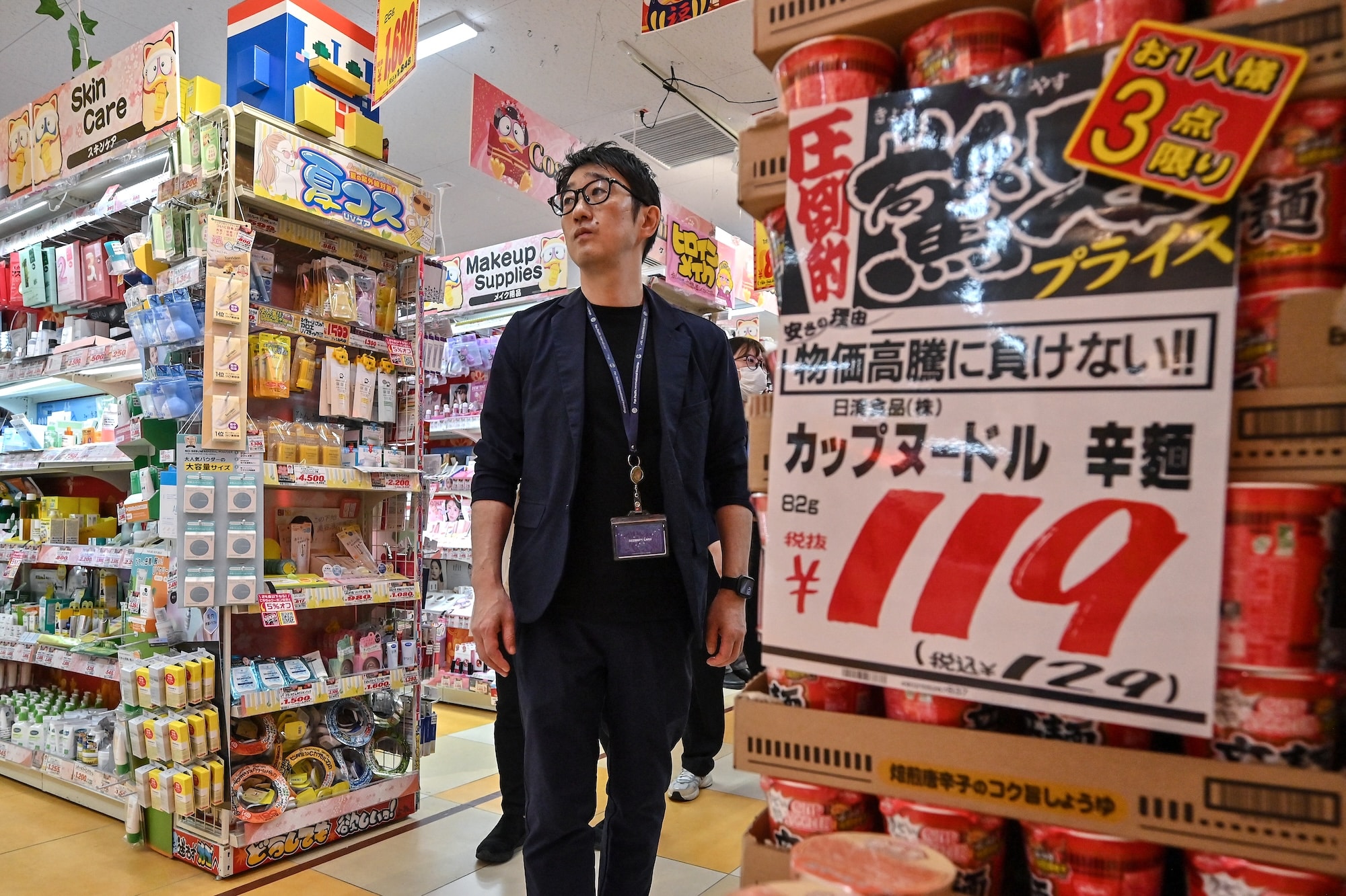 This photo taken on April 21, 2025 shows Motoki Hata, inbound support department manager, walking past cup noodles (R) for sale during an interview with AFP at a branch of Japanese discount retailer Don Quijote, also known overseas as Don Don Donki, in the Shibuya district of central Tokyo. In the narrow, crowded aisles of a department store in Tokyo's Shibuya district, hundreds of tourists rush to fill their baskets with snacks, gadgets, and souvenirs of all kinds, fuelling sales at Don Quijote, the king of Japanese discount stores. (Photo by Richard A. Brooks / AFP) / TO GO WITH AFP STORY JAPAN-TOURISM-ECONOMY-RETAIL,FOCUS BY CAROLINE GARDIN AND ATISH PATEL